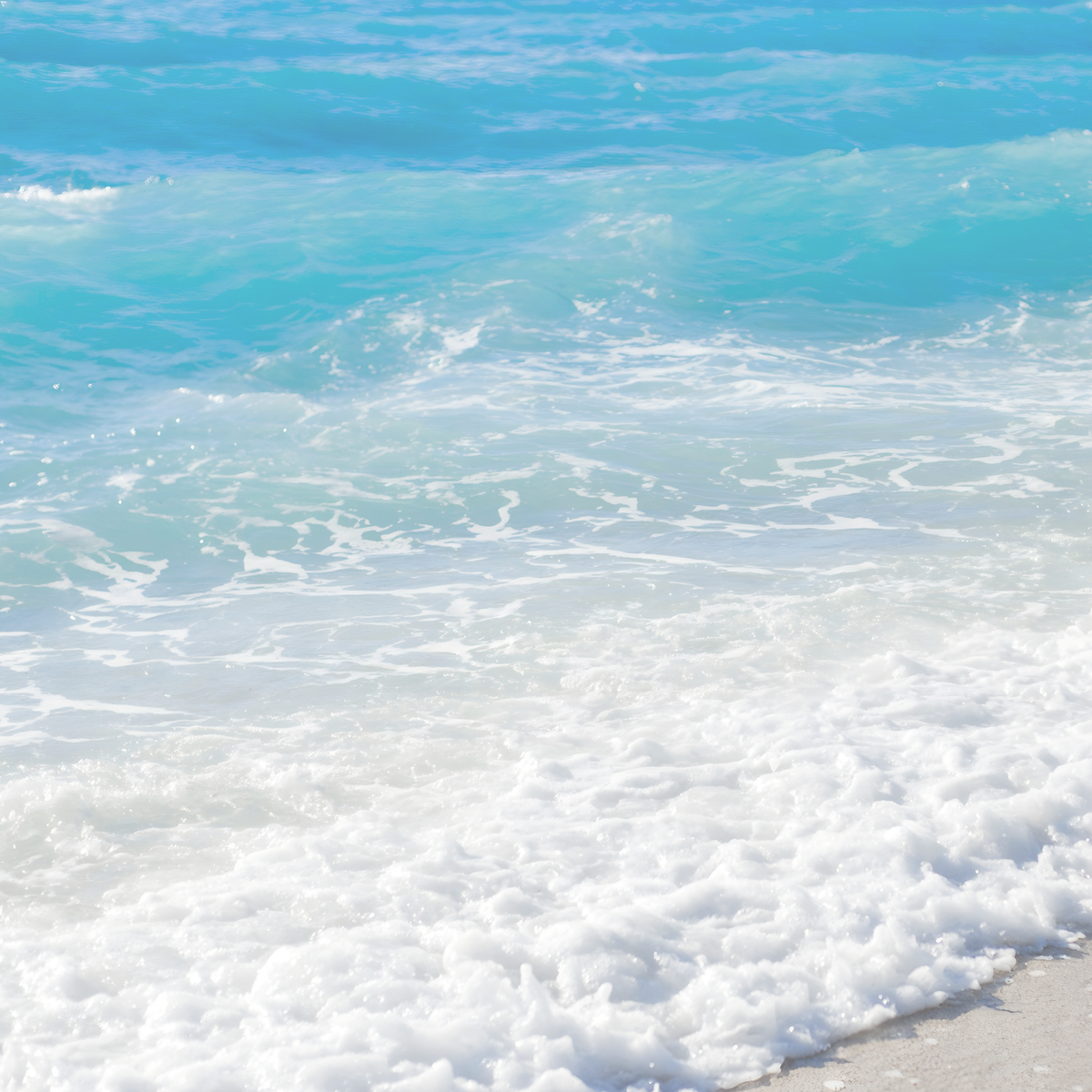 Turquoise waves washing onto a sandy shore, inspiration for the By the Sea Scent Series.