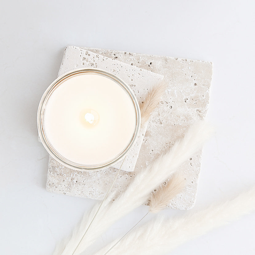 Overhead view of a creamy wax candle on pale stone with dried grasses.